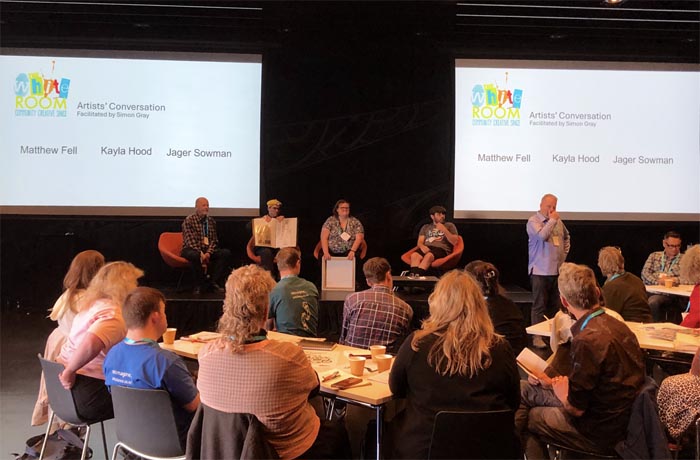The White Room presentation: from left, Simon Grey, Matthew Fell, Kayla Hood and Jagar Sowman seated on chairs and facing the audience. Behind them are two screens with The White Room logo and artists' names